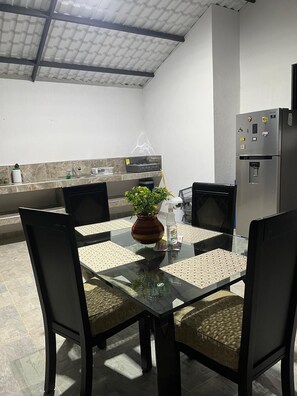 A modern kitchen with a glass dining table, chairs, a refrigerator, and a plant.