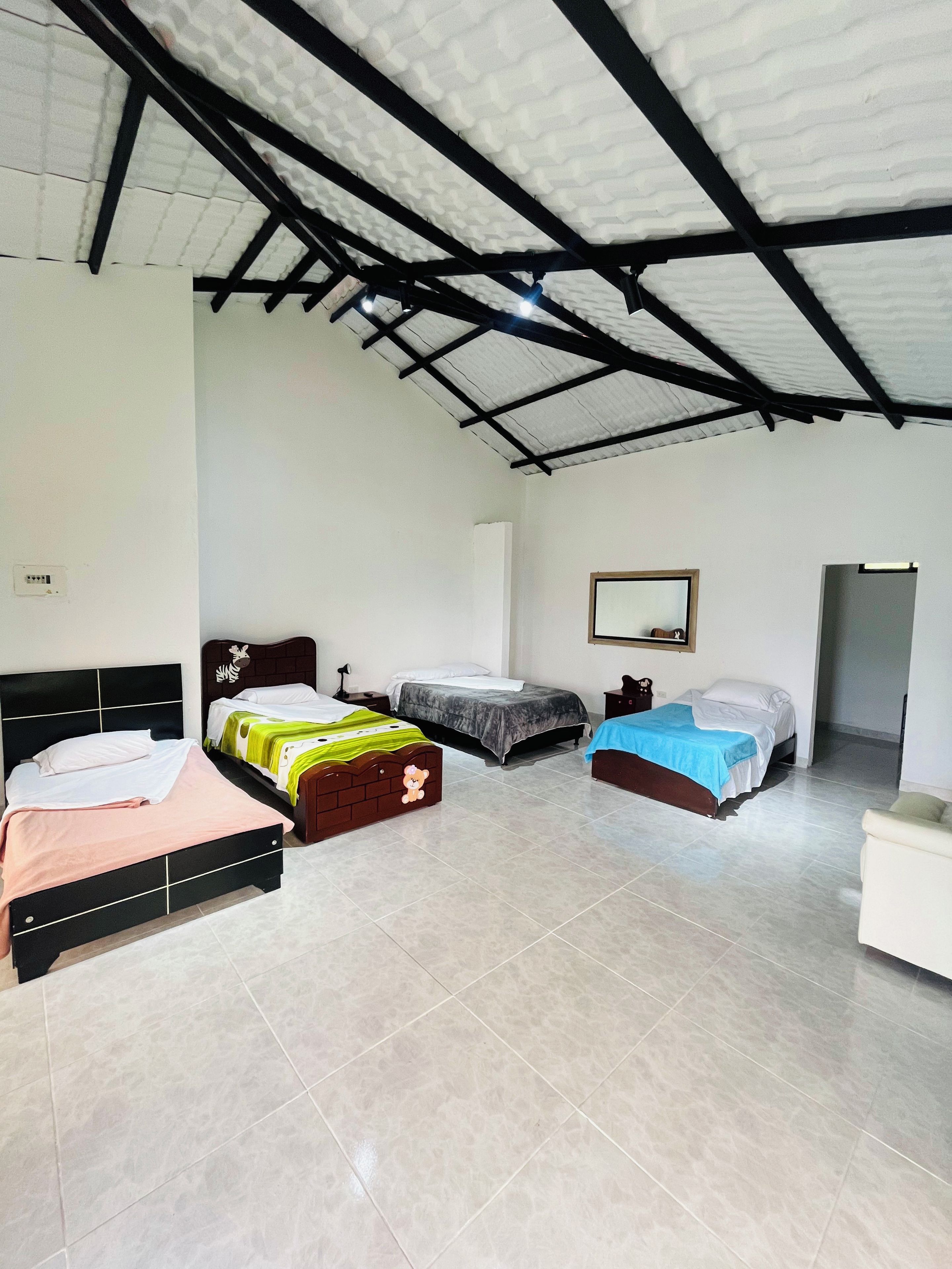 Ein Zimmer mit drei Betten, einer weißen Wand, einer Decke mit schwarzem Metallfachwerk und einem gefliesten Boden.