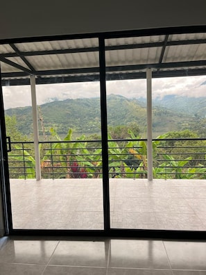 Una habitación con un amplio ventanal corredero que da a un balcón con vistas a un paisaje montañoso.