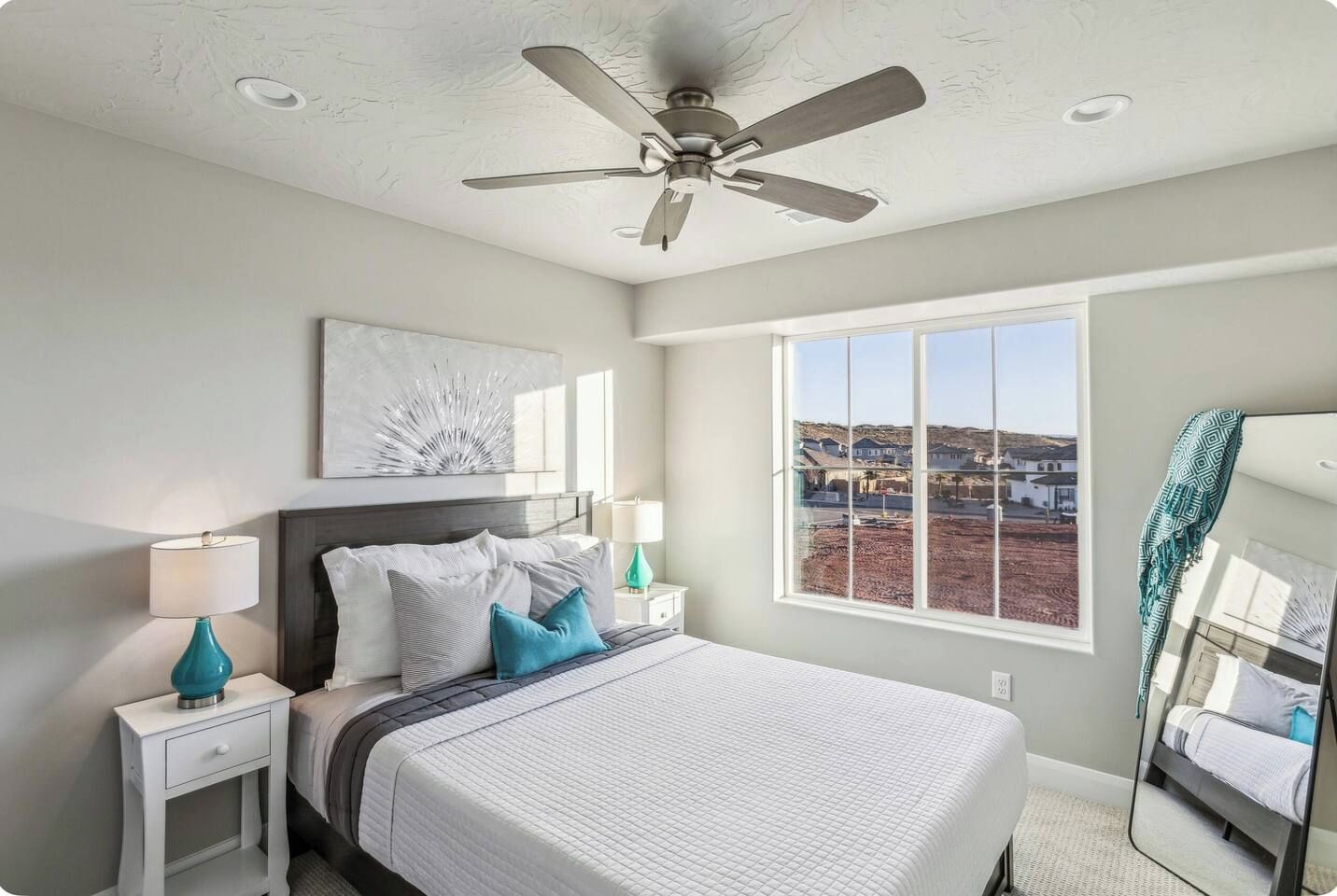 A bedroom with a bed, nightstands, a ceiling fan, a large window, and a view of a landscape.