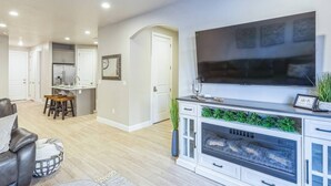 A modern living room with a fireplace, a flat-screen TV, and a dining area with a kitchen in the background. - Heated Pool & Pickleball - Beautiful 3BR Home Near Zion (Washington)