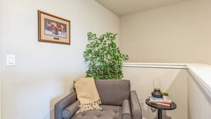 A corner room with a gray armchair, a small table with books and a lamp, a framed picture on the wall, and a green plant. - Heated Pool & Pickleball - Beautiful 3BR Home Near Zion (Washington)