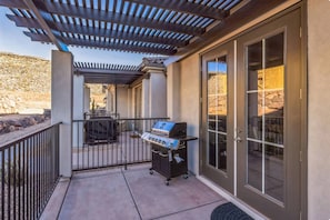Eine überdachte Terrasse mit Grill, einer Tür zu einer Steinmauer und Blick auf die umliegende Landschaft.