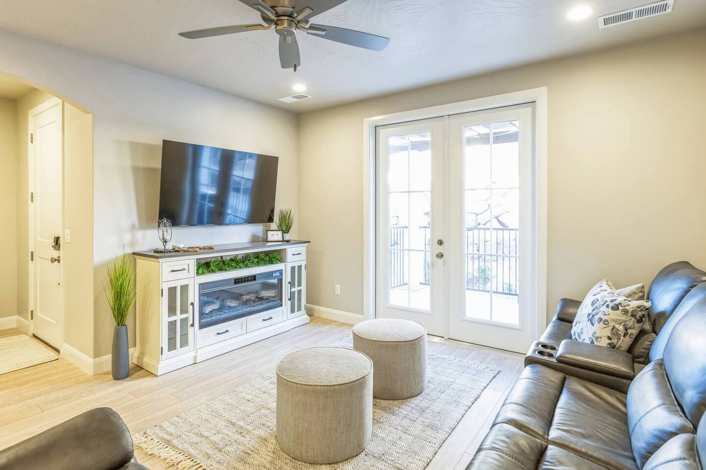 A living room with a flat-screen TV, a sofa, ottomans, and a ceiling fan.