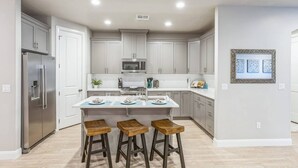 A modern kitchen with white cabinetry, a stainless steel refrigerator, a microwave, and a central island with stools. - Heated Pool & Pickleball - Beautiful 3BR Home Near Zion (Washington)