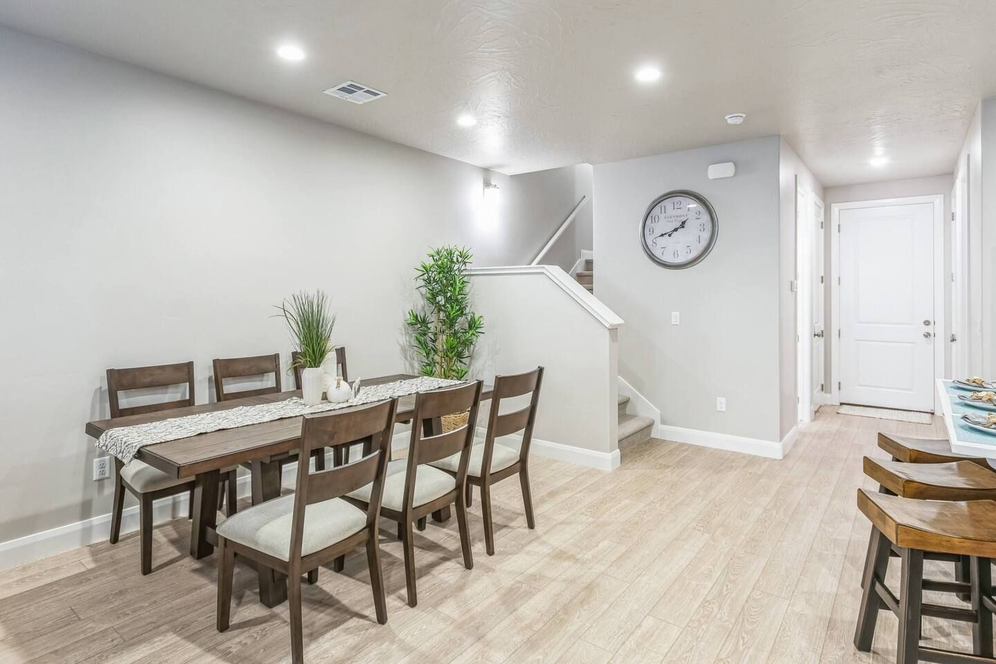 A dining area with a wooden table and chairs, a clock on the wall, and a staircase leading to another level.