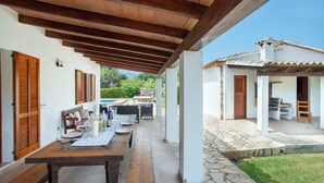 An outdoor patio with a wooden table set for dining, a pool in the background, and a stone pathway leading to a building. - Countryside Retreat in La Font, A/C, Private Pool, Large Garden - 15mins Walk to Old Town Pollenca! (Pollença)