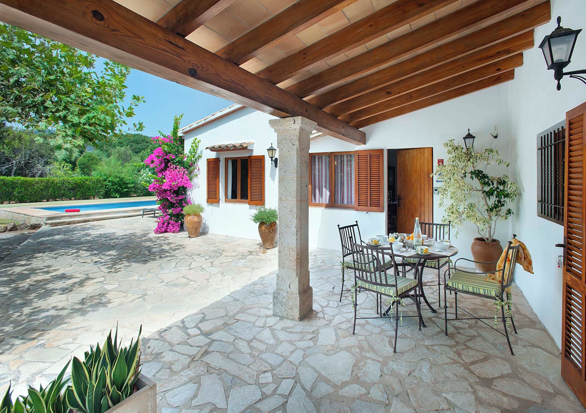 A covered patio with stone flooring, a dining table with chairs, and potted plants.