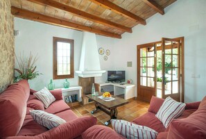 A living room with a sofa set, a fireplace, a television, and a dining table with a fruit bowl. - Countryside Retreat in La Font, A/C, Private Pool, Large Garden - 15mins Walk to Old Town Pollenca! (Pollença)