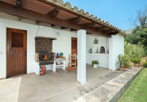 A patio with a brick fireplace, a wooden door, and a white wall with shelves. - Countryside Retreat in La Font, A/C, Private Pool, Large Garden - 15mins Walk to Old Town Pollenca! (Pollença)