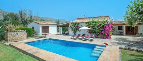 Une piscine avec un espace patio, du mobilier d’extérieur et un bâtiment blanc doté d’un toit en tuiles.