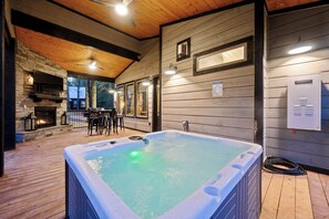 Ein Außenbereich mit Whirlpool, Steinofen, Holzterrasse und überdachter Sitzecke.