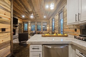 A modern log cabin interior with a kitchen, dining area, and a fireplace. - Champagne Bliss | 2 King Suites + Hot Tub (Broken Bow)
