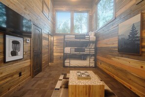 Interior de una cabaña con literas, paredes de madera, una ventana y un cuadro enmarcado.