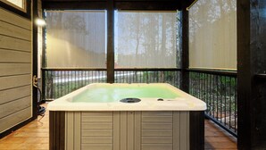 Ein Whirlpool in einem überdachten Außenbereich mit einer Holzterrasse und Blick auf Bäume.