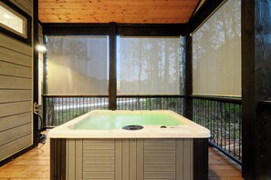 A hot tub in a covered outdoor area with a wooden deck and a view of trees. - Champagne Bliss | 2 King Suites + Hot Tub (Broken Bow)