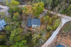 A house surrounded by trees with a dirt road nearby. - Champagne Bliss | 2 King Suites + Hot Tub (Broken Bow)