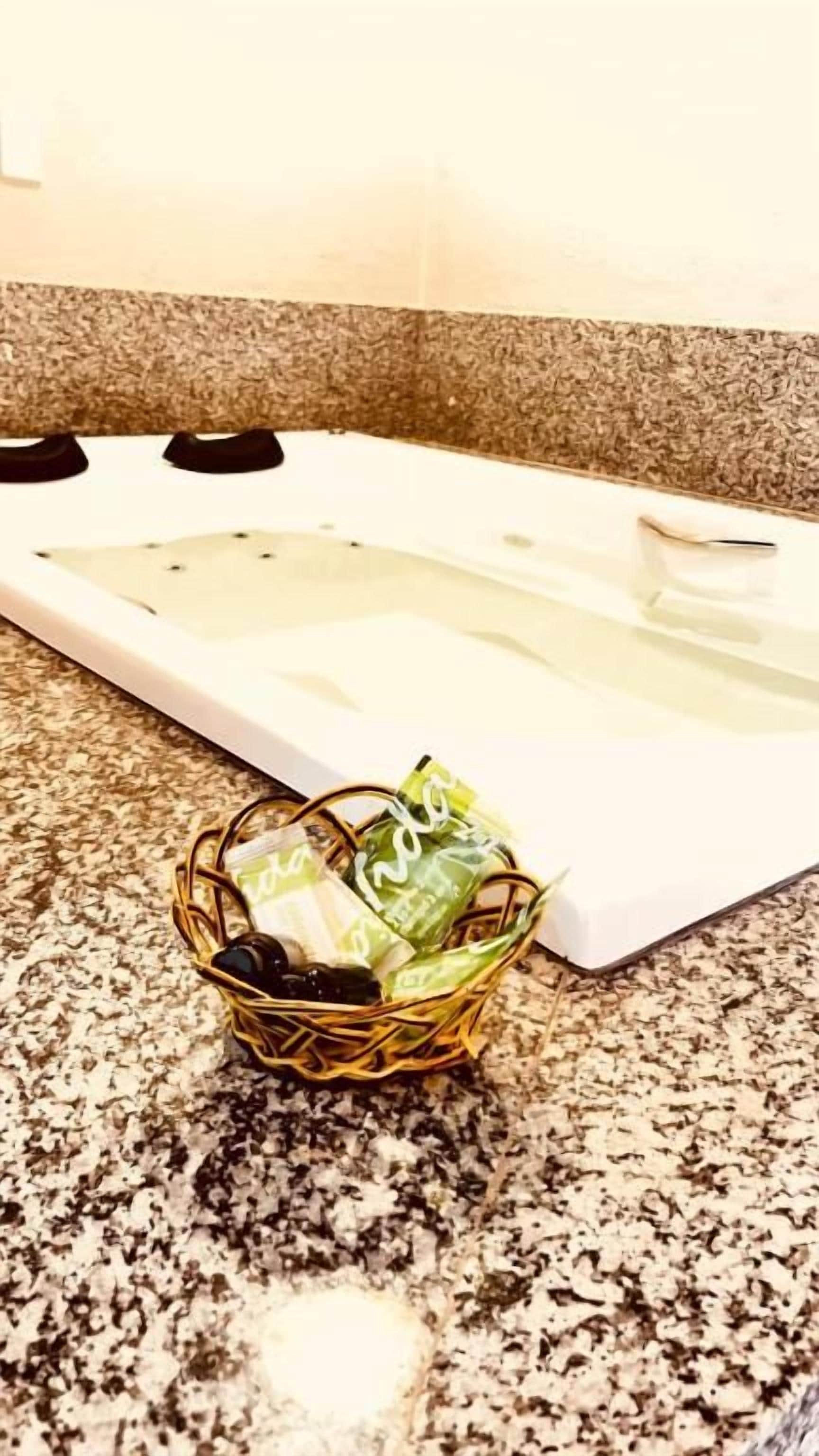 Casa de banho com bancada de granito, uma banheira branca e cestaria com artigos de higiene pessoal.