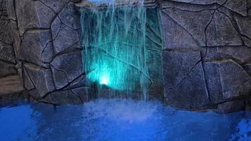 Een zwembad met een waterval, omringd door rotswanden.