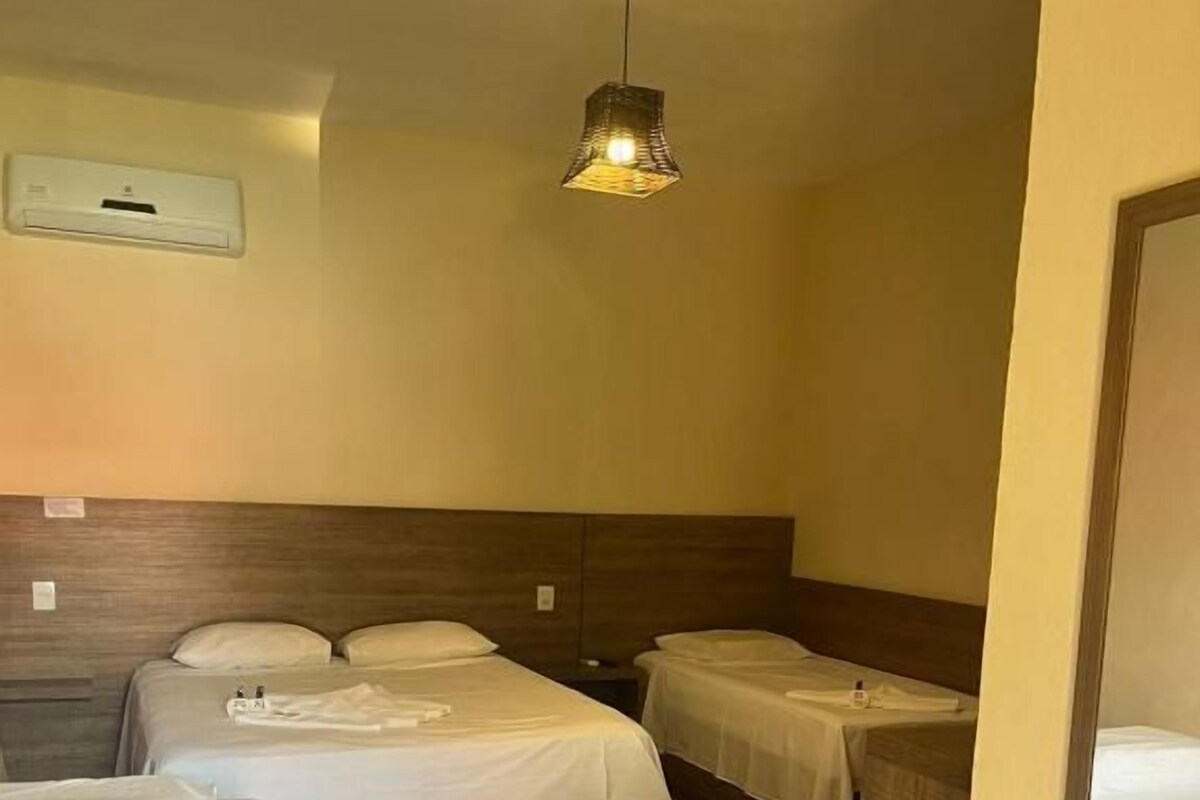 A hotel room with two beds, a wooden headboard, a hanging light fixture, and a small table.