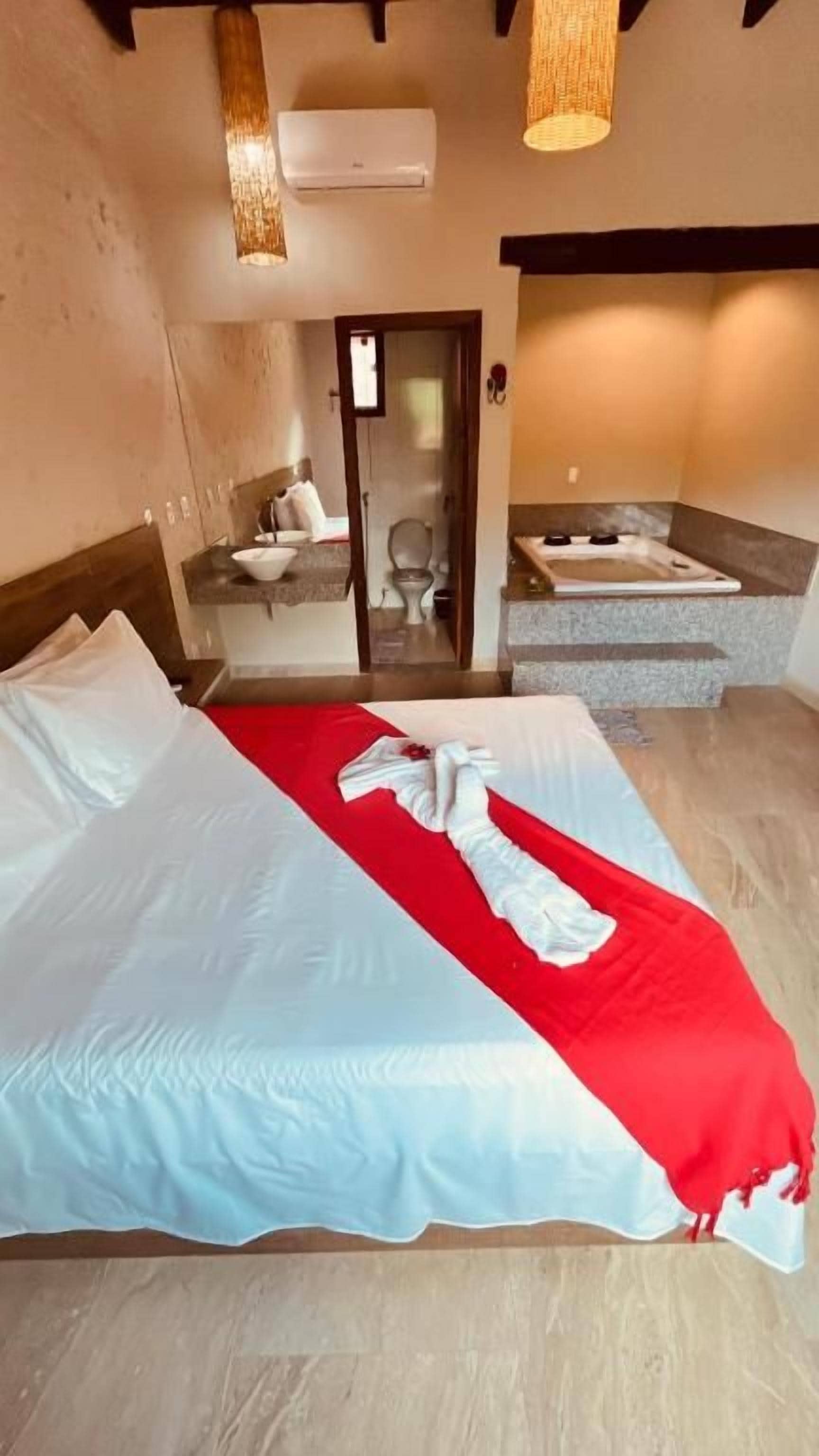 A hotel room with a bed, a red and white blanket, a bathroom with a bathtub, and a mirror.