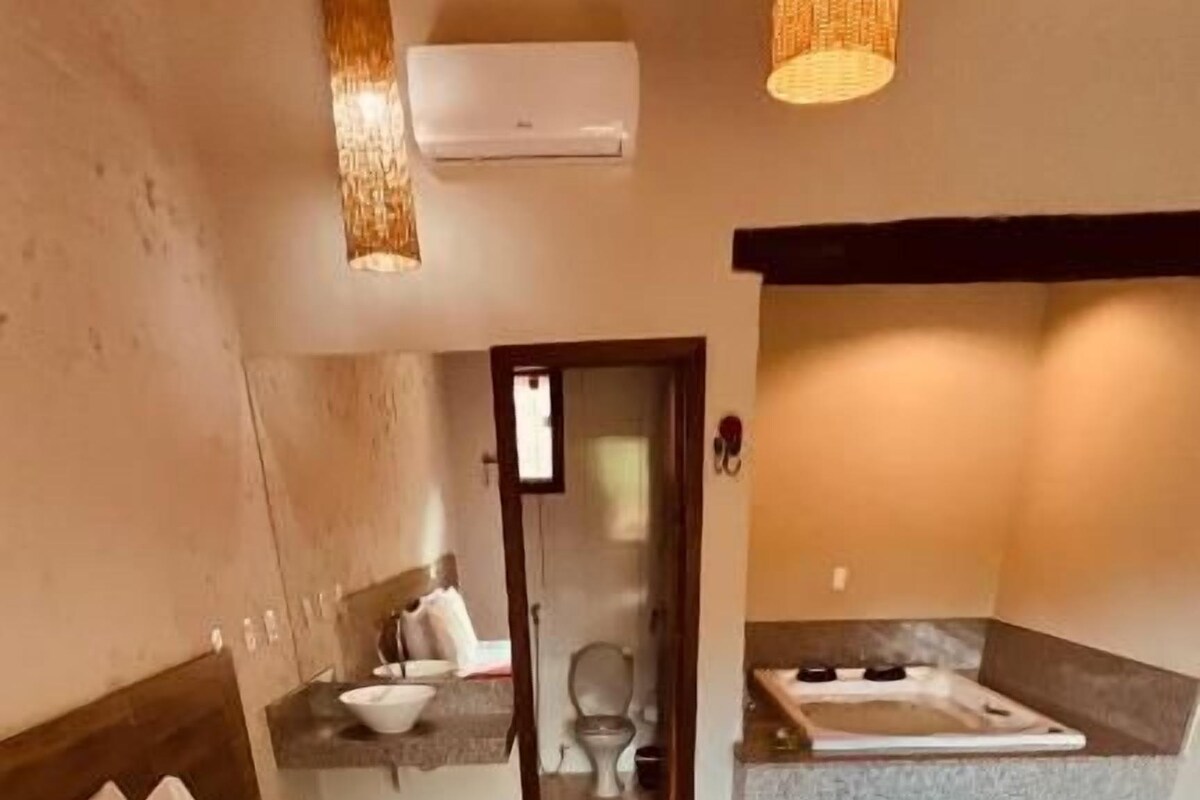 A hotel room with a bed, a red and white blanket, a bathroom with a bathtub, and a mirror.