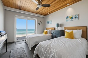 Een hotelkamer met twee bedden, een bureau en uitzicht op het strand.