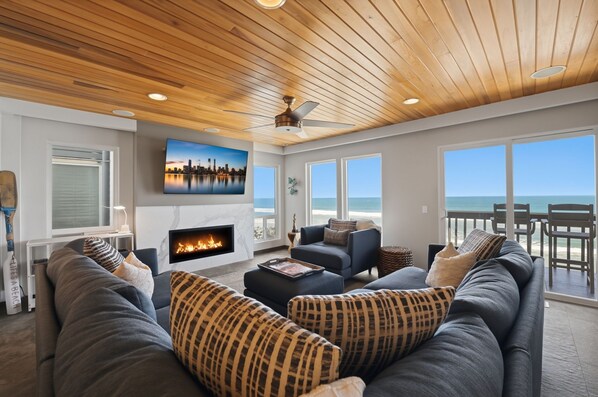 Een ruime woonkamer met een open haard, comfortabele zithoek en grote ramen met uitzicht op het strand.