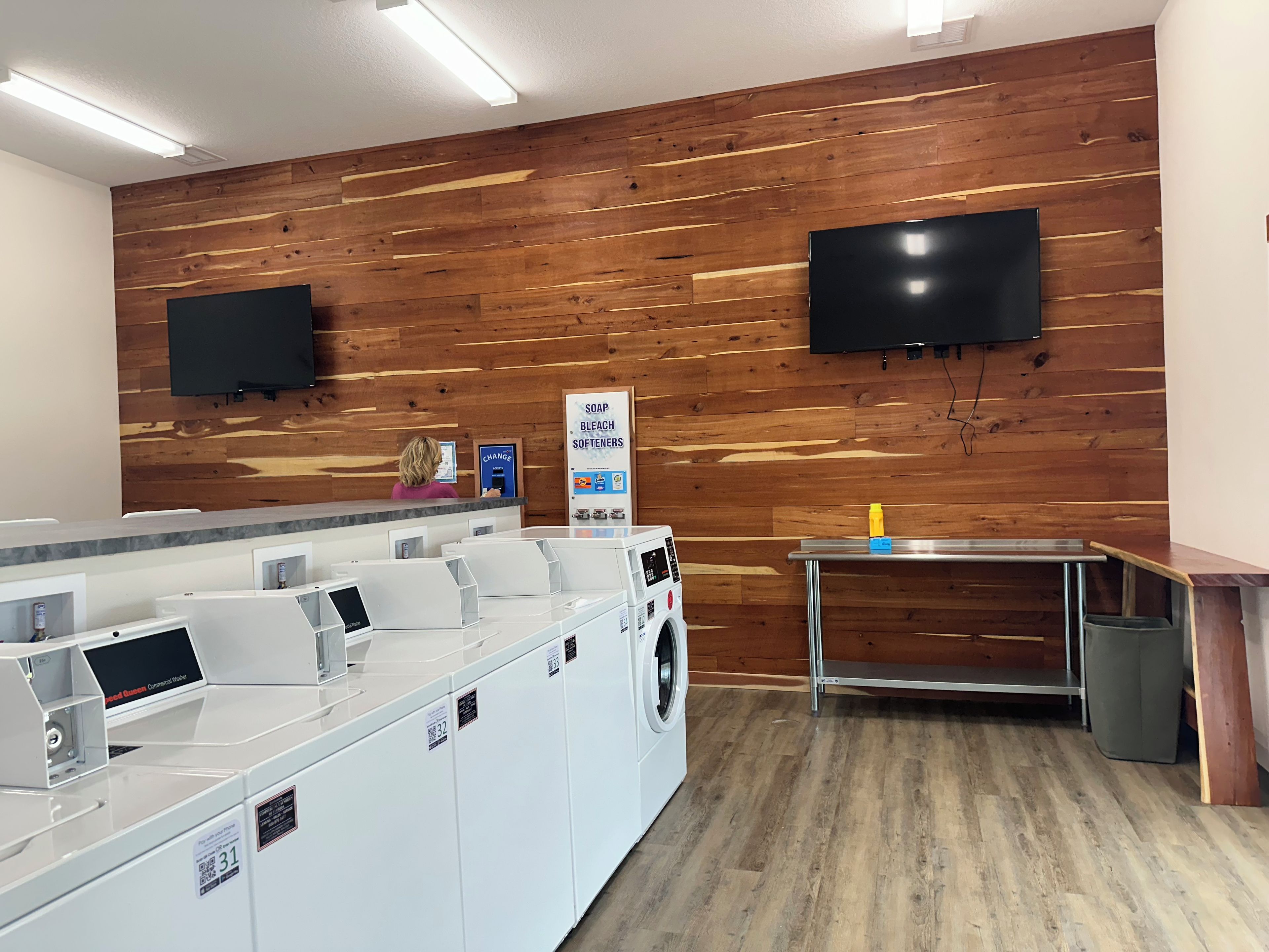 A laundry facility with multiple washing machines, a change station, and a television mounted on the wall.
