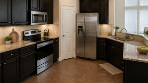 Una cocina moderna con armarios oscuros, electrodomésticos de acero inoxidable y suelo de baldosas.