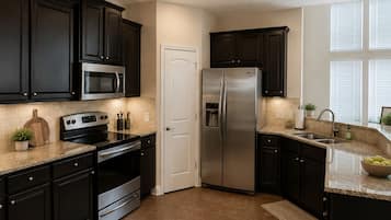 A modern kitchen with dark cabinets, stainless steel appliances, and a tiled floor.