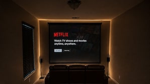 Sala de cine en casa con una pantalla grande mostrando la interfaz de Netflix, asientos de cuero reclinables y piso alfombrado.