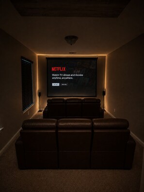Et hjemmebioværelse med stort skærm der viser Netflix, læderlænestole og et tæppe belagt gulv.