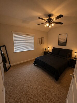 A bedroom with a bed, a ceiling fan, a window with blinds, bedside lamps, and framed artwork on the wall. - Spacious 3BR Retreat Theater, Games & Workspace (Plano)