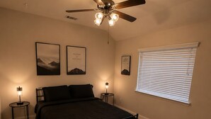 Un dormitorio con una cama, dos mesitas de noche, un ventilador de techo y una ventana con persianas.