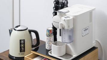 Una cafetera, un hervidor y un cajón con cápsulas de café sobre una mesa de madera.