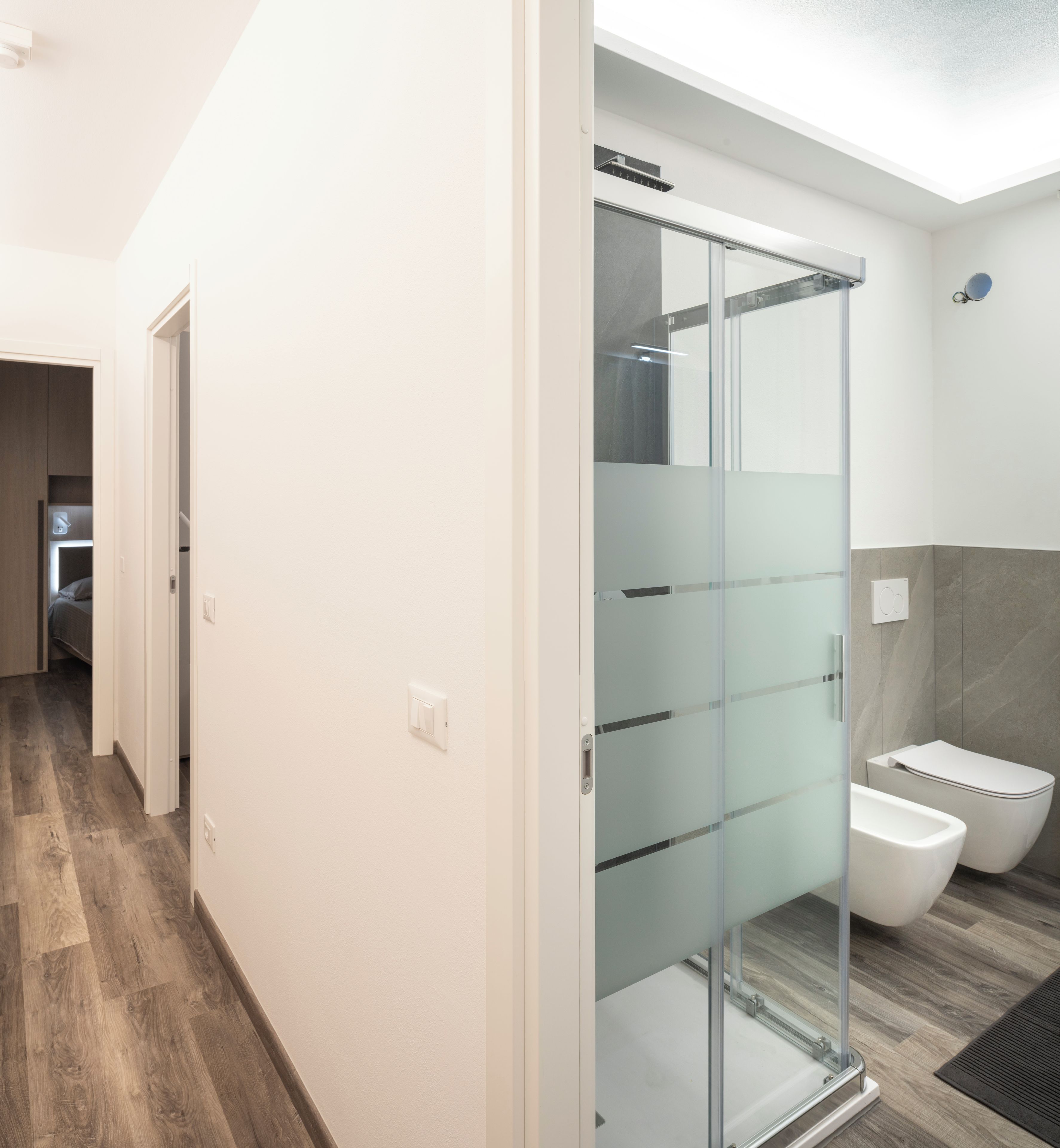 Un bagno moderno con cabina doccia in vetro, un water e pavimento in legno.