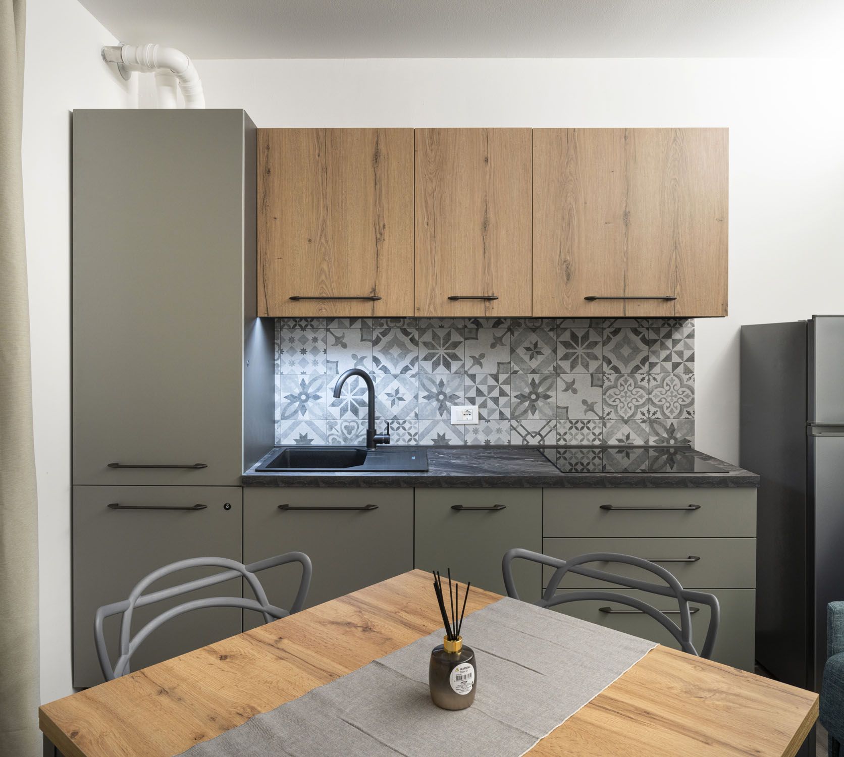 A modern kitchen with grey cabinets, a black faucet, and a patterned backsplash.