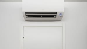 Una puerta blanca con un aire acondicionado de pared encima. Hay dos dispositivos de pared a cada lado de la puerta, uno en cada lado.