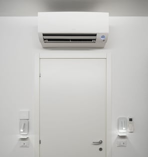 Une porte blanche, avec un climatiseur fixé au mur juste au-dessus. De chaque côté de la porte, on peut voir deux appareils fixés au mur, un de chaque côté.