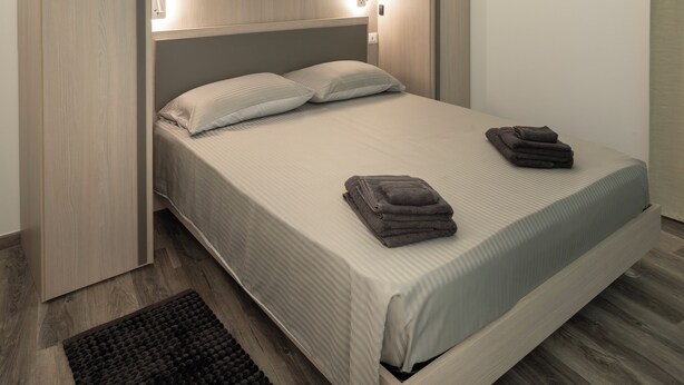 Una cama con cabecera, lámparas de noche, mesita de noche y una alfombra oscura.