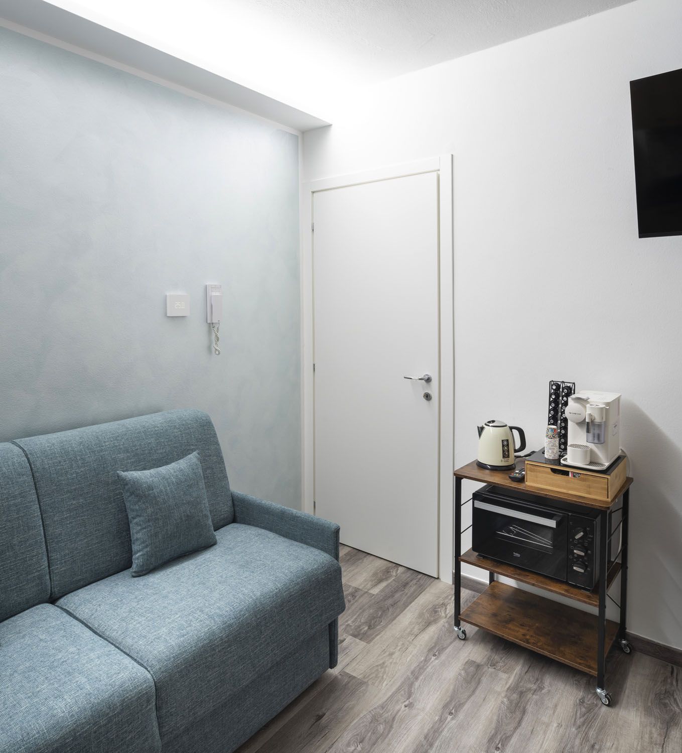 A modern room with a grey sofa, a coffee machine, and a TV on the wall.