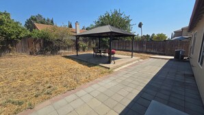 Un giardino con patio, barbecue e zona salotto coperta.