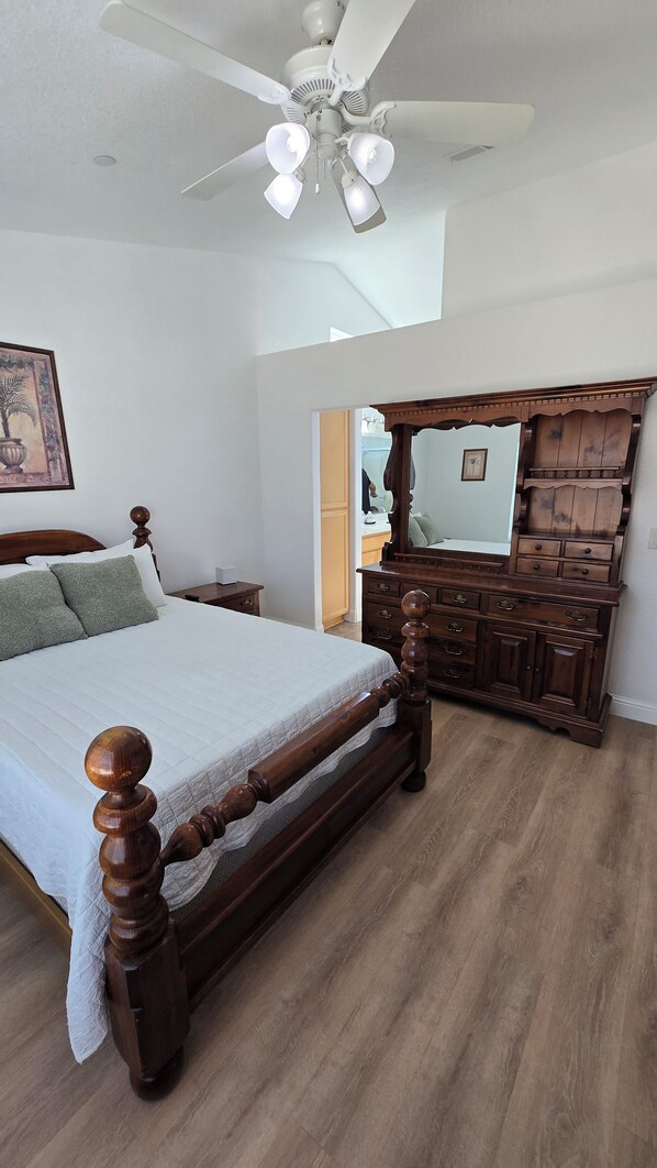 A bedroom with a wooden bed, a ceiling fan, a dresser, and a mirror.
