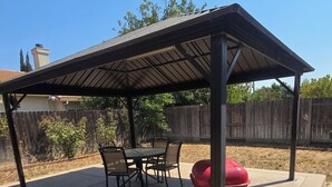 Un patio esterno coperto con una griglia barbecue, un tavolo con sedie e un recinto in legno sullo sfondo.
