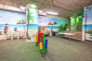 A beach-themed room with a mural, chairs, a table, and exercise equipment. - Amazing Ocean View Condo with Waterpark and Pool (Myrtle Beach)