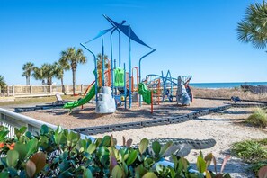 A playground with slides and climbing structures, surrounded by sand and palm trees. - Amazing Ocean View Condo with Waterpark and Pool (Myrtle Beach)
