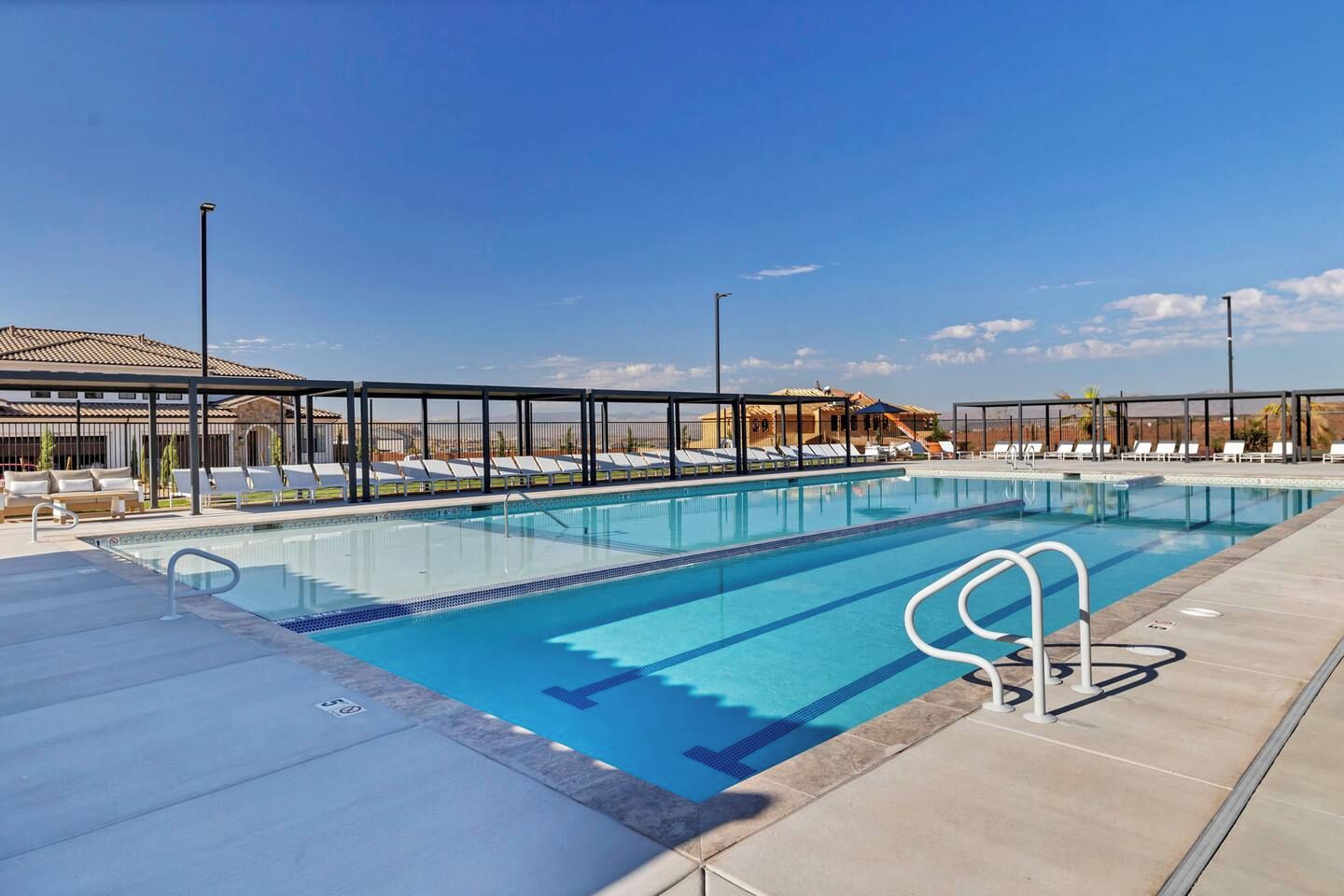 Ein Swimmingpool mit Liegestühlen und einer überdachten Liegefläche, umgeben von Gebäuden.