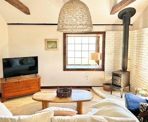 A cozy living room with a television, a woven light fixture, a fireplace, and a window with a view.