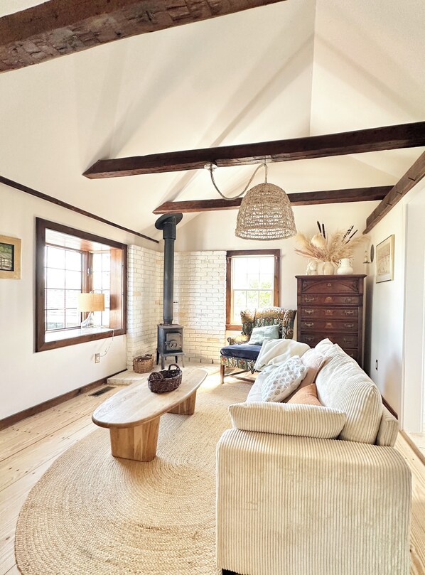 A rustic living room with exposed wooden beams, a stone fireplace, a woven light fixture, and a comfortable sofa.